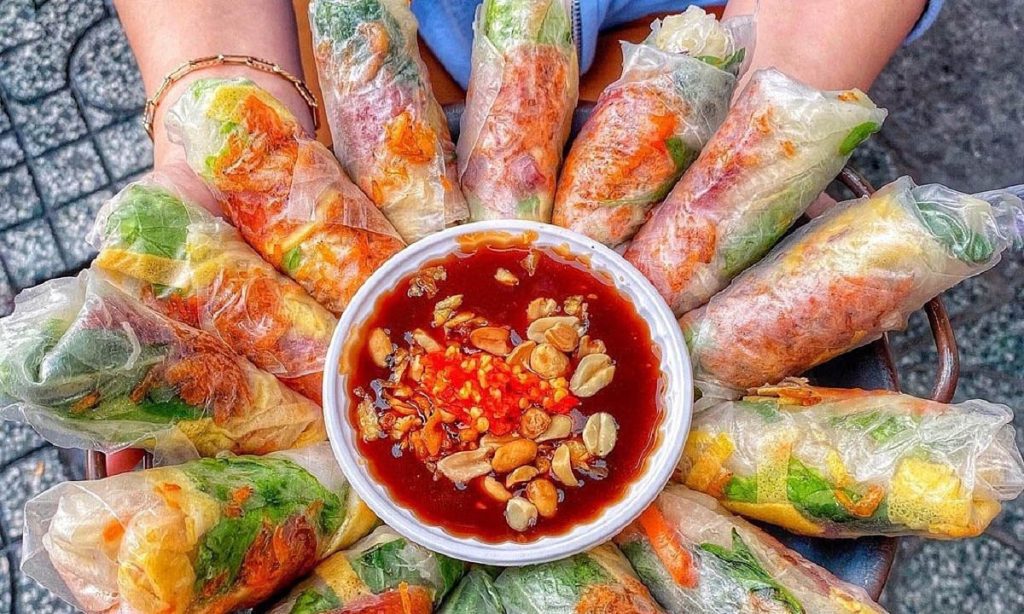 Đĩa bò bía cuốn nhiều màu sắc với nhân rau sống, lạp xưởng, trứng và củ sắn, ăn kèm chén nước chấm ngọt mặn rắc lạc rang và ớt băm hấp dẫn.
