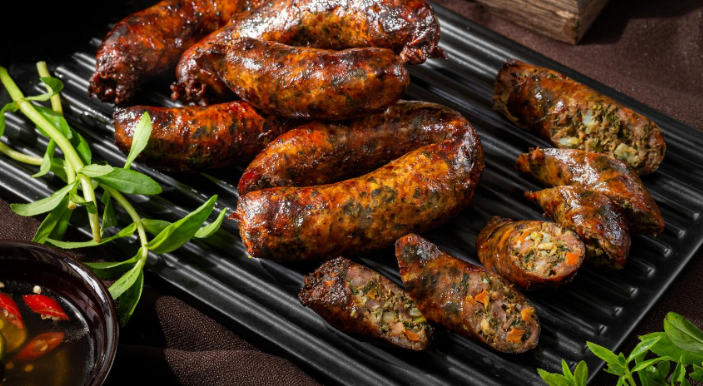 Dồi sụn nướng vàng ruộm, cắt khoanh, bày trên đĩa cùng rau thơm và chén nước chấm ớt tỏi.