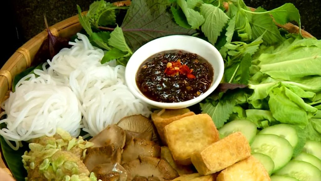 Mẹt bún đậu chay đầy đủ với bún tươi, đậu hũ chiên vàng, nấm, rau sống xanh mát và chén mắm chay đậm đà, trang trí thêm ớt đỏ tạo điểm nhấn, bày biện trên nền lá chuối truyền thống.