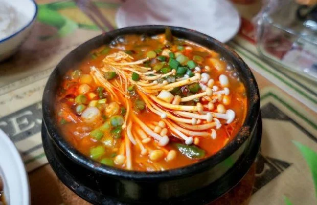 Tô canh kim chi chay nóng hổi với màu đỏ hấp dẫn, trang trí nấm kim châm và hành lá, món ăn cay nồng, giàu dinh dưỡng thích hợp cho thực đơn chay.