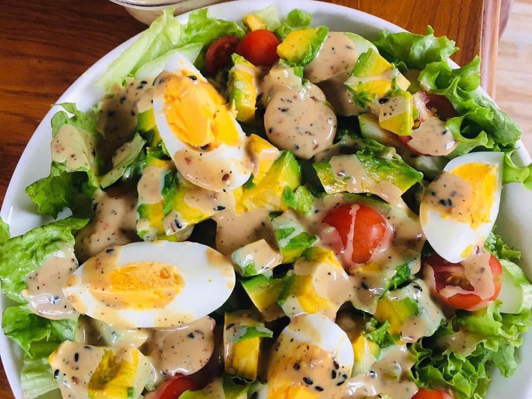 Đĩa salad trộn sốt mè rang hấp dẫn với rau xà lách tươi, cà chua bi, bơ, trứng luộc và lớp sốt mè béo ngậy phủ đều, món ăn thanh mát lý tưởng cho thực đơn chay tháng 7 âm lịch.