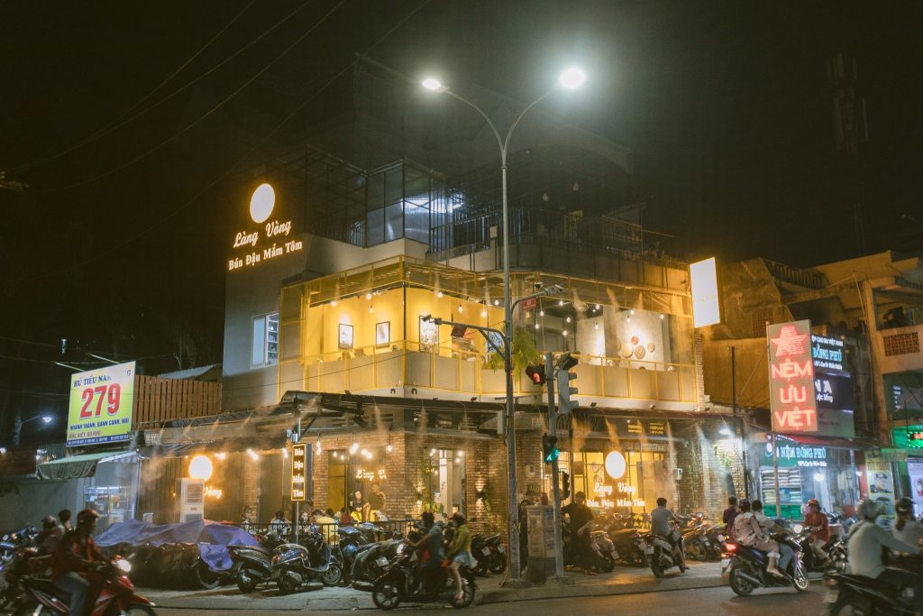 Quán bún đậu mắm tôm Làng Vòng tại TP.HCM nhìn từ bên ngoài vào buổi tối, không gian sáng đèn vang nổi bật, thu hút đông khách và xe cộ tấp nập trước cửa.